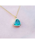 Tilted heart emerald pendant with halo diamonds on an 18K yellow gold chain.