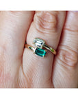 A close-up of a gold ring with two emerald-cut green gemstones worn on a person's finger.
