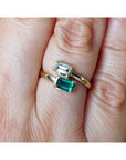 A close-up of a gold ring with two emerald-cut green gemstones worn on a person's finger.