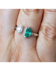 A close-up of a hand wearing a toi et moi emerald and diamond ring in white gold.