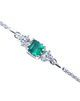 Topside view of a white gold bracelet with a square natural emerald and diamonds on a white background.
