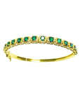 the topside view of a gold bangle bracelet with round cut natural emeralds on a white background.