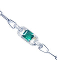 A white gold paperclip bracelet with a natural emerald and diamonds on a topside view.