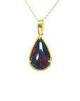 Teardrop-shaped black opal pendant on a gold chain on topside view against a white background.