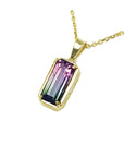 Gold necklace with a multicolored tourmaline gemstone pendant on a left side profile view.