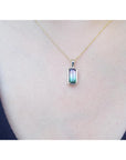 Gold necklace with a pendant featuring a multicolored tourmaline gemstone on a person's neck.