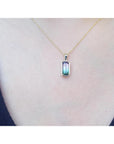 Gold necklace with a pendant featuring a multicolored tourmaline gemstone on a person's neck.