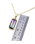Gold necklace with a multicolored natural tourmaline gemstone pendant next to a ruler for scale on a white background.