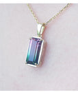 Necklace with a colorful tourmaline pendant on a light pink skin background.