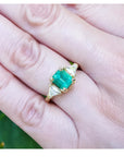 1.51 ct. emerald and trillion cut diamonds ring in 18k gold on a hand.
