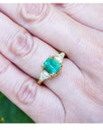 1.51 ct. emerald and trillion cut diamonds ring in 18k gold on a hand.