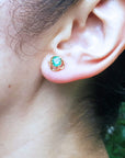 Close-up of a woman's ear wearing a natural tulip emerald stud earrings in a blurred natural background.