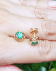14k yellow gold tulip emerald stud earrings on a hand against a natural background.