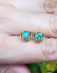 Yellow gold tulip emerald stud earrings held between fingers on a light skin background.