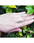 Colombian emerald tulip stud earrings in 14K yellow gold, worn on a hand against green foliage.