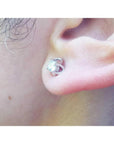 White gold tulip stud earring with a round natural diamond, worn on an ear.