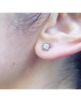 White gold tulip stud earring with a round diamond, worn on an ear.
