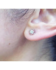 White gold tulip stud earring with a round diamond, worn on an ear.