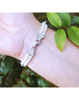 Pearl bracelet on a wrist with green leaves in the background.