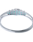 A white gold emerald bangle bracelet displaying its underside view.
