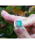 Vintage ring with a natural colombian emerald held between fingers against a blurred natural background.