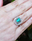 Hand wearing a vintage ring with a colombian emerald against a leafy background.