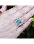 Hand wearing a vintage ring with a colombian emerald against a leafy background.