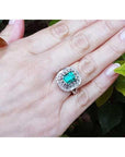 Hand wearing a vintage ring with a colombian emerald against a leafy background.