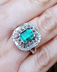 Ring with an emerald and diamond vintage ring on a hand.