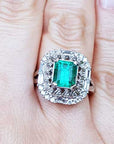 A vintage Colombian emerald ring with accent diamonds on a finger.