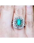 A vintage Colombian emerald ring with accent diamonds on a finger.