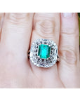 A vintage Colombian emerald ring with accent diamonds on a finger.