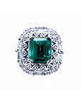 This vintage-style Colombian emerald ring features a square emerald cut, encircled by sparkling diamonds, and crafted from 14k white gold.