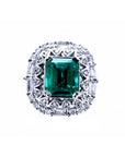 This vintage-style Colombian emerald ring features a square emerald cut, encircled by sparkling diamonds, and crafted from 14k white gold.