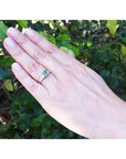 Hand wearing a natural colombian emerald ring with accent diamonds against a green leafy background.