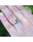 A square natural colombian emerald ring on a hand against a blurred green background.