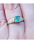 A 14k yellow gold natural colombian emerald ring for women on a finger.
