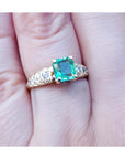 A 14k yellow gold natural colombian emerald ring for women on a finger.