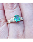 A 14k yellow gold natural colombian emerald ring for women on a finger.
