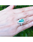 Anillo de oro blanco 14k con esmeralda colombiana corte pera de 3.35 ct rodeada de diamantes en mano.