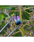 Vibrant red-orange and bluish-green watermelon tourmaline, rectangular emerald cut, held by tweezers.