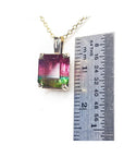A natural watermelon tourmaline gemstone pendant on a chain with a ruler for scale on a white background