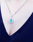 Pear cut emerald necklace with double diamond halo, 18K white gold chain, worn on a person.