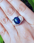 Ring with a blue Welo opal on a person's finger against a natural background