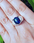 Ring with a blue Welo opal on a person's finger against a natural background