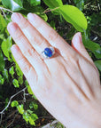 Hand wearing a silver ring with a blue opal against a green leafy background