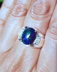 Silver ring with a colorful black opal on a person's finger
