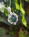 Opal pendant with silver frame on a chain against a green leafy background