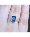 Blue sapphire ring white gold showcasing a rich deep blue hue. Accented with natural diamonds along the sides, on a finger.