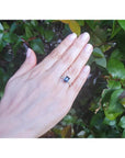 18K white gold ring with a radiant-cut blue sapphire and diamond accents on a woman's hand.